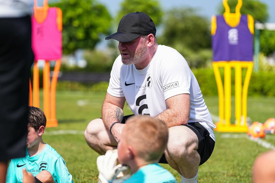 Wayne Rooney crouching with young players during a Football Escape camp